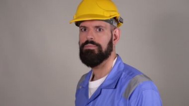 Sarı kask selamlıyor sakallı adam işçi, gri arka planda elini sallayarak