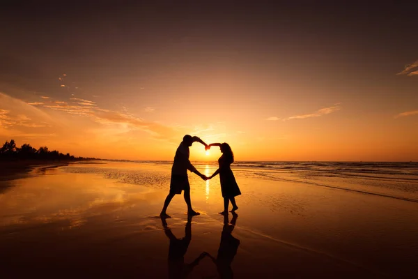 Silhouette of couple making heart shape with arms on beach at sunset — Stock Photo, Image
