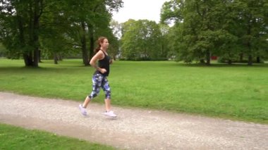 Yavaş çekim genç spor kadın yeşil parkta koşuyor.