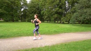 Yavaş çekim genç spor kadın yeşil parkta koşuyor.