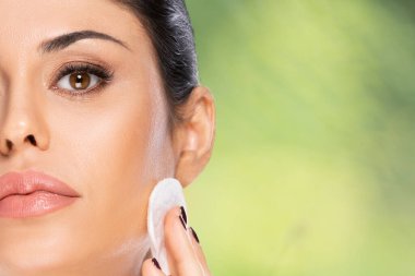 Pamuklu yastıklı, yeşil arkaplanı bulanık ve fotokopi alanı olan güzel esmer kadın. Sağlık ve güzellik kavramı