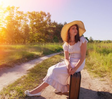 Bir bavul bir ülke yolda yorgun oturan şapkalı kız.