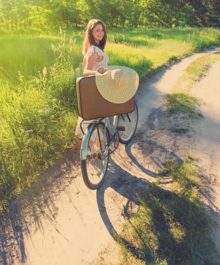 kız bisiklet üzerinde bir bavulla kırsal bir yolda yaz günde rides