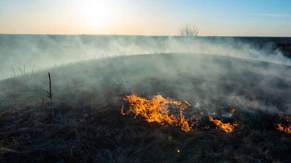 smoke and fire, burning dry grass on the hillside. Villager they set fire to dry grass so that young grass would grow to feed animals. Early spring in the countryside.