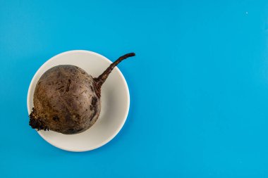 Kırmızı pancar otunun kökü mavi arka planda beyaz bir tabakta yatar. Yemek pişirmek..