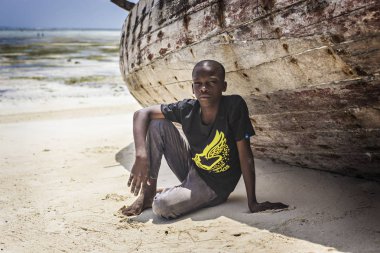 Sahilde ahşap tekne yakın oturan ve kameraya, Zanzibar, Tanzanya arıyorum Genç Afrikalı çocuk