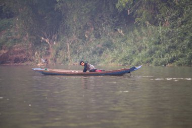 LUANG PRABANG, LAOS - Nisan 2019: Mekong Nehri 'ndeki geleneksel uzun tahta teknede Lao adamı, Luang Prabang, Laos