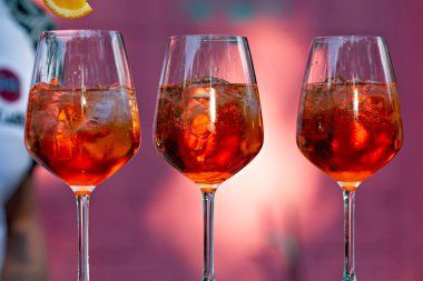 Üç bardak Aperol Spritz. Pembe arka planda yakın plan.