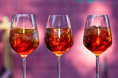 Üç bardak Aperol Spritz. Pembe arka planda yakın plan.
