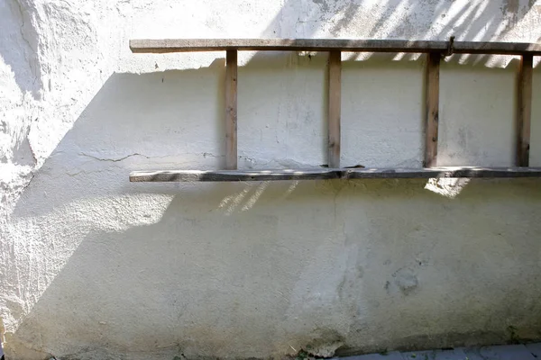 Old ladder hanging on white wall of a rustic coun tryhouse with shadow. — Stock Photo, Image