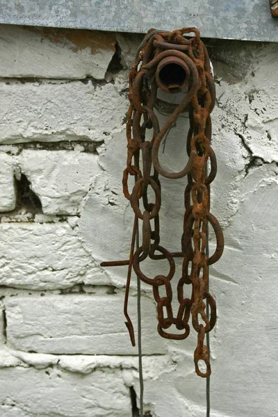 Velha corrente enferrujada pendurada perto de uma parede de tijolo pintado de branco . — Fotografia de Stock