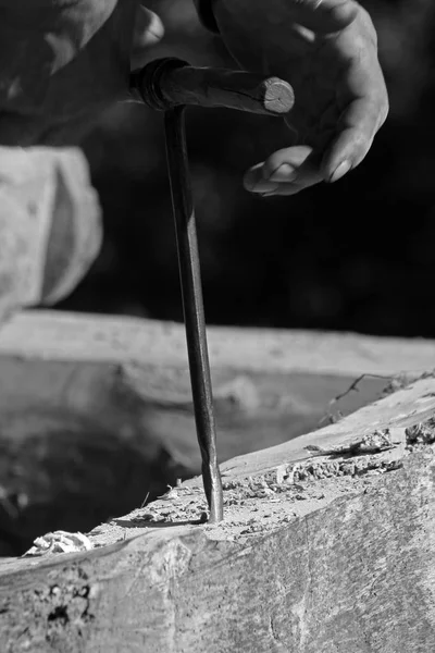 Le mani operaie fanno un buco con un trapano a mano in un pezzo di legno. Nero una foto bianca . — Foto Stock