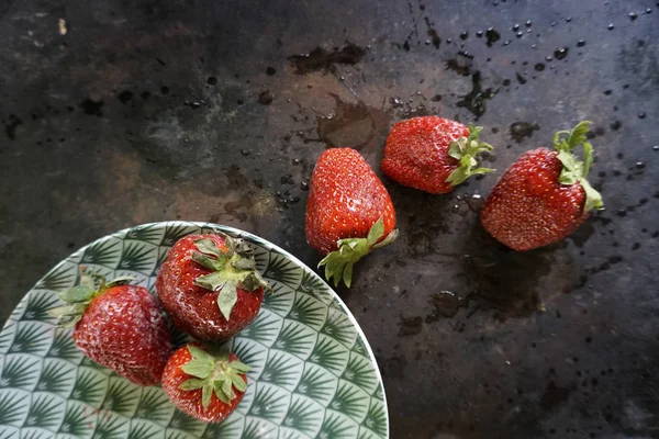 Groupe de fraises sur plaque en céramique motif vert et serviette en linène blanche sur fond sombre avec spl d'eau, cendres et gouttes . — Photo