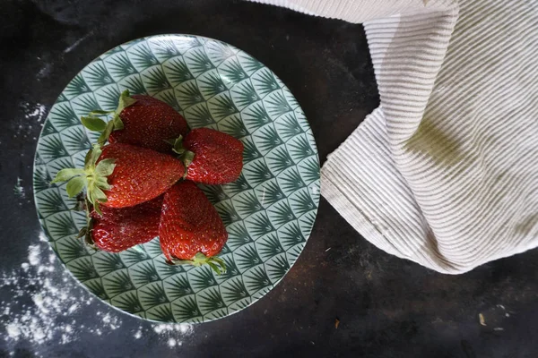 Groupe de fraises sur plaque en céramique motif vert et serviette en linène blanche sur fond sombre . — Photo