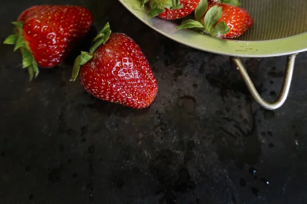 大金属筛里新鲜的草莓。在黑暗的背景上溅水滴. — 图库照片
