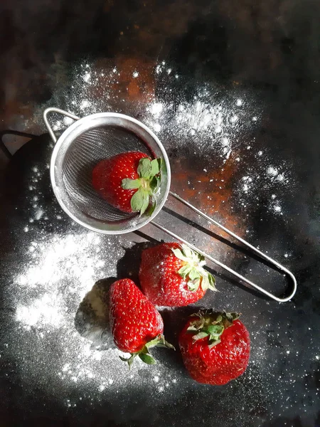 Fresh strawberries in a small metal sieve. with powdered icing sugar on a dark background. — Stock Photo, Image