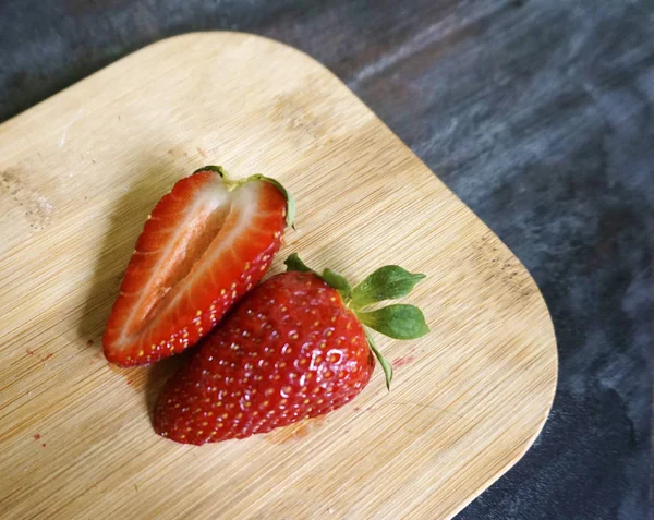 Strawberry cut in half on wooden cutting board on dark background. — Stock Photo, Image
