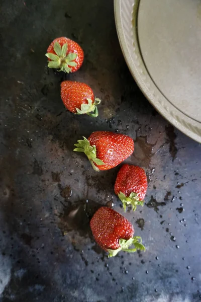 Fraises rouges mûres avec gouttes d'eau éclaboussures et assiette sur fond sombre. Vue du dessus . — Photo