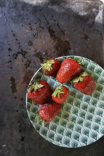 Group of strawberries on green pattern ceramic plate and white linene napkin on dark background with water spl,ash and drops. — Stock Photo, Image