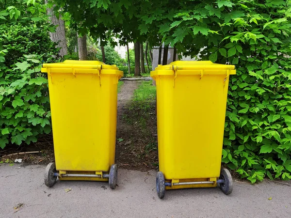 Two yellow garbage containers on the side of the street.