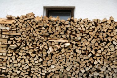 Rustik bir evin beyaz duvarının yanında yığılmış odun.