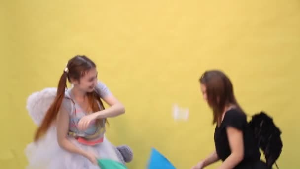 Two friends have fun fighting pillows in the form of an angel and a demon — Stock Video