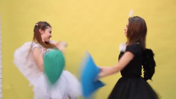 Two friends have fun fighting pillows in the form of an angel and a demon — Stock Video