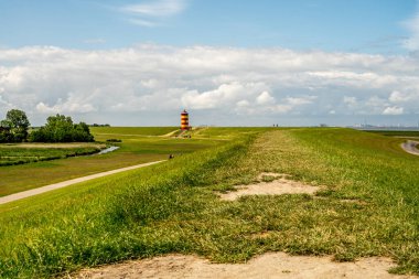 view on Pilsum lighthouse in East Frisia with tourists walking around the dike and taking photographs clipart