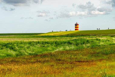 Doğu Frizya 'daki Pilsum deniz fenerinin manzarasında hendekte dolaşıp fotoğraf çeken turistler var.