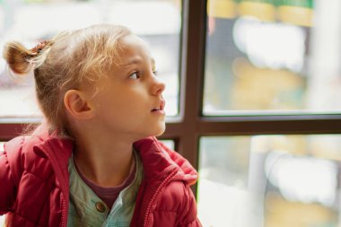 Küçük bir kız pencereden yan bakar
