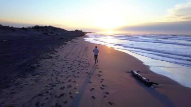 Hava dron genç çekici adam sahilde güneş doğarken koşu ile kaydırma. Egzersiz uygulama çalışan fitness ve sağlıklı yaşam konsepti.