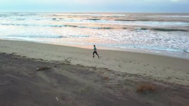 Hava dron genç çekici adam sahilde güneş doğarken koşu ile kaydırma. Egzersiz uygulama çalışan fitness ve sağlıklı yaşam konsepti.