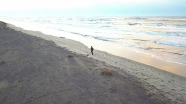 Hava dron genç çekici adam sahilde güneş doğarken koşu ile kaydırma. Egzersiz uygulama çalışan fitness ve sağlıklı yaşam konsepti.