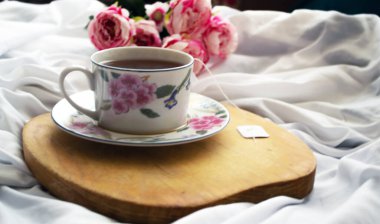 Yatakta çay, dinlenmek için hazır. Arka tarafta şakayıklar var.