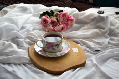 Yatakta çay, dinlenmek için hazır. Arka tarafta şakayıklar var.