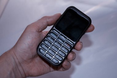 Bir adamın elini masanın üzerinde eski bir buton telefon tutuyor.
