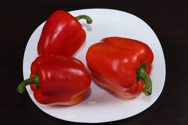 Hala yemek ile hayat. Üç büyük tatlı Bulgar kırmızı biber koyu bir arka plan ile beyaz servis plaka üzerinde masada yalan.