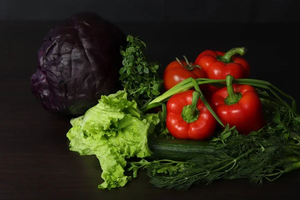 Hala sebze yiyecekleri olan bir hayat. Kompozisyon kırmızı lahana ve beyaz lahana merkezinde, büyük Olgun kırmızı biber önünde, tatlı ve sulu, yanı sıra kırmızı olgun domates ve karanlık bir arka planda otlar ile taze yeşil salatalık