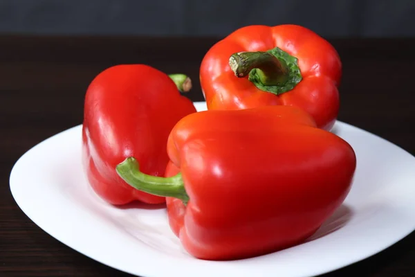 Hala yemek ile hayat. Üç büyük tatlı Bulgar kırmızı biber koyu bir arka plan ile beyaz servis plaka üzerinde masada yalan.