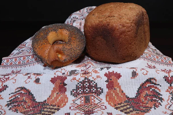 Güzel kokulu ve sağlıklı ev yapımı ekmek çıtır simit çavdar ve buğday unu kavrulmuş kahverengi kabuğu ile haşhaş tohumu ile serpilir, Horozları ile işlemeli havlu üzerinde yalan. Arka planı karanlık.