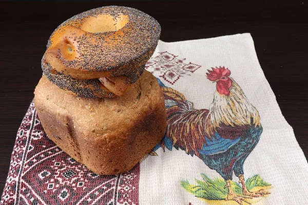 Güzel kokulu ve sağlıklı ev yapımı ekmek çıtır simit çavdar ve buğday unu kavrulmuş kahverengi kabuğu ile haşhaş tohumu ile serpilir, Horozları ile işlemeli havlu üzerinde yalan. Arka planı karanlık.