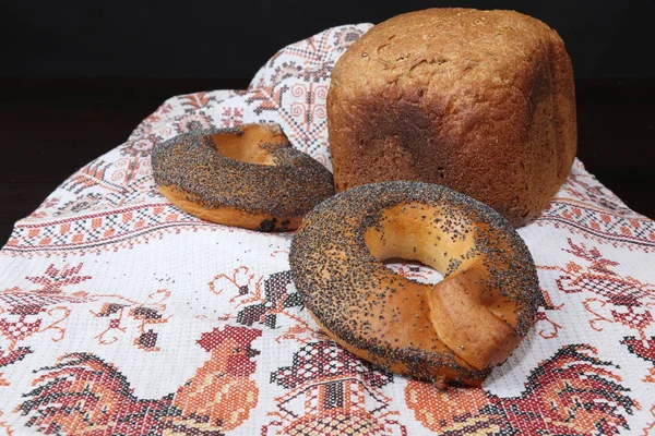 Güzel kokulu ve sağlıklı ev yapımı ekmek çıtır simit çavdar ve buğday unu kavrulmuş kahverengi kabuğu ile haşhaş tohumu ile serpilir, Horozları ile işlemeli havlu üzerinde yalan. Arka planı karanlık.