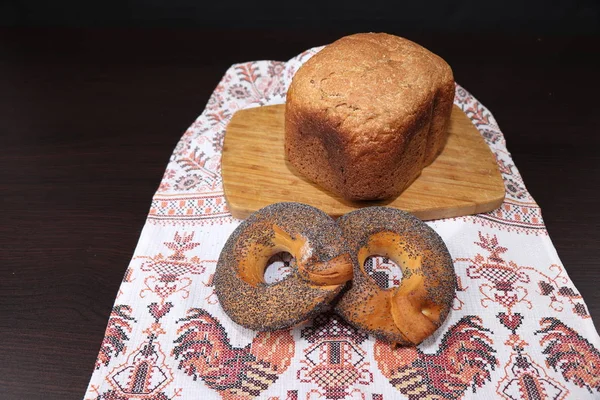 Güzel kokulu ve sağlıklı ev yapımı ekmek çıtır simit çavdar ve buğday unu kavrulmuş kahverengi kabuğu ile haşhaş tohumu ile serpilir, Horozları ile işlemeli havlu üzerinde yalan. Arka planı karanlık.