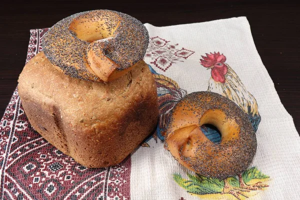 Güzel kokulu ve sağlıklı ev yapımı ekmek çıtır simit çavdar ve buğday unu kavrulmuş kahverengi kabuğu ile haşhaş tohumu ile serpilir, Horozları ile işlemeli havlu üzerinde yalan. Arka planı karanlık.