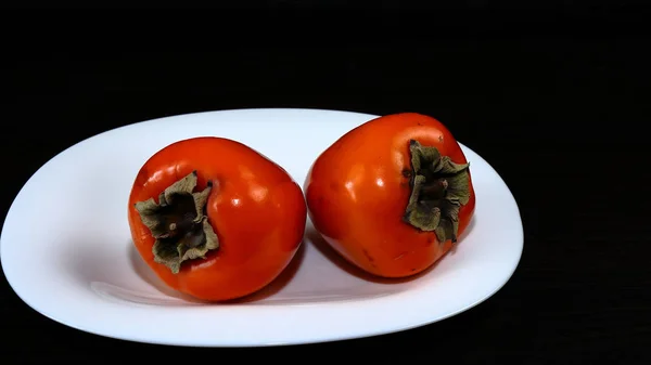 Tropikal meyvelerin hala hayatı. Koyu bir masada beyaz servis plaka üzerinde olgun turuncu Persimmon meyve.