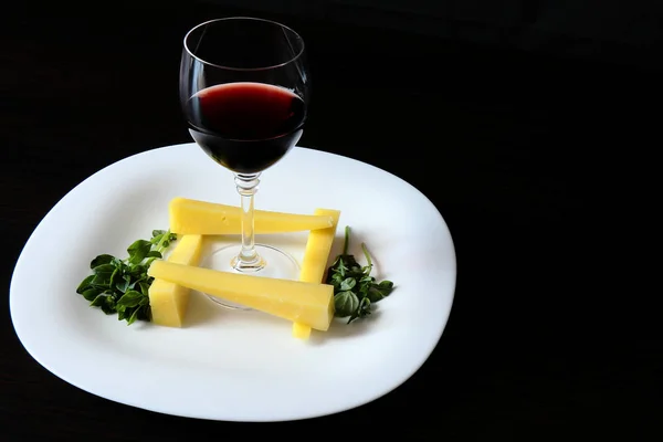 Sert peynir ve yeşil Basil bir delikanlı bir snack ile bir servis beyaz plaka üzerinde Vintage kırmızı şarap ile şarap cam. Plaka karanlık masada..