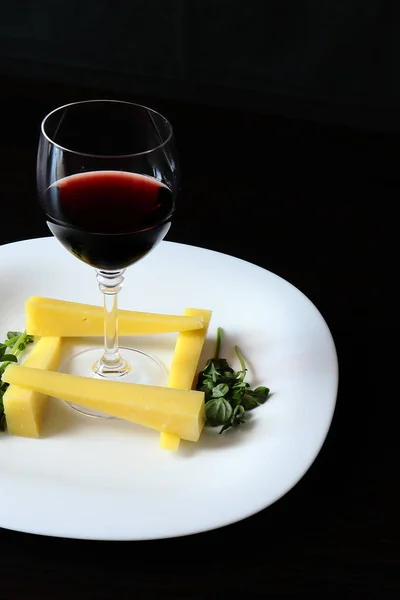 Sert peynir ve yeşil Basil bir delikanlı bir snack ile bir servis beyaz plaka üzerinde Vintage kırmızı şarap ile şarap cam. Plaka karanlık masada..