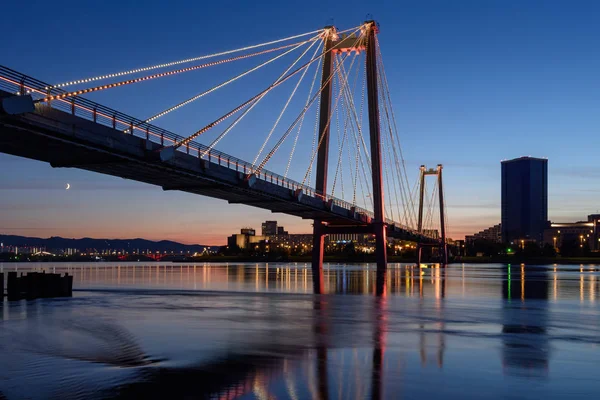 Krasnoyarsk gece manzaralı yaya köprüsü. Ufuktaki şehir ışıklarının manzarası.