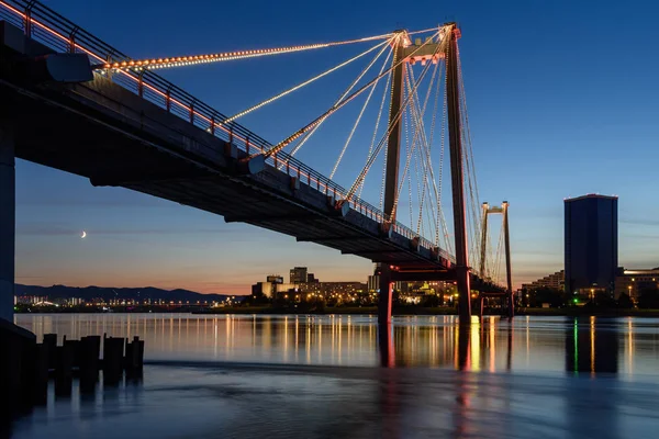Gece şehrinin Krasnoyarsk manzarası ve Yenisei üzerindeki yaya köprüsü. Ufuktaki şehir ışıklarının manzarası.
