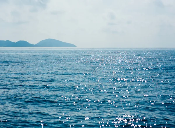 Mavi deniz yüzeyi, parlak dalgalar, arka planda dağlar, güzel deniz manzarası. 